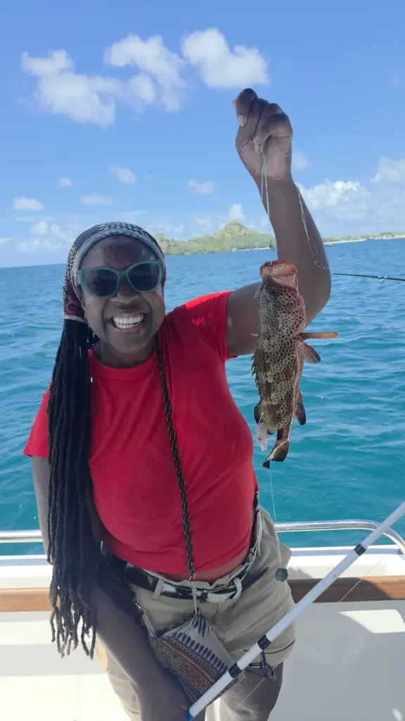 A smiling guest holding up a spotted red hind caught on the boat