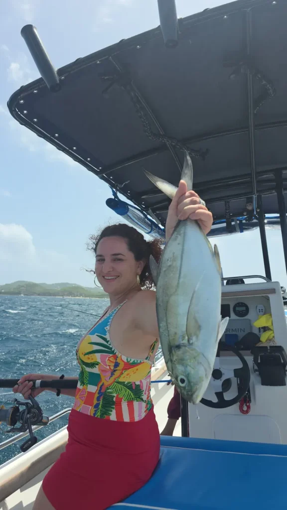 A guest holding up a large silver jack on board, with the green coastline behind