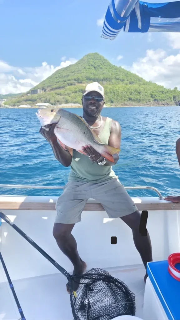 A guest holding a large mutton snapper in front of a green hill