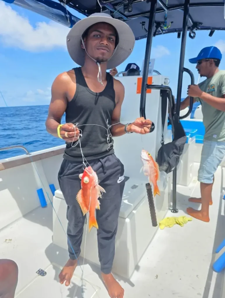 A guest holding two bright red snappers on board