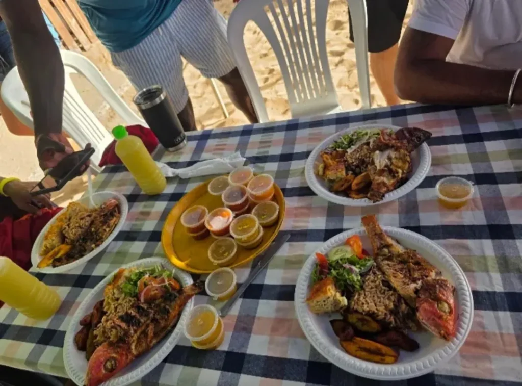 Plates of grilled fish with rice, salad and fried plantain on a checked tablecloth by the beach